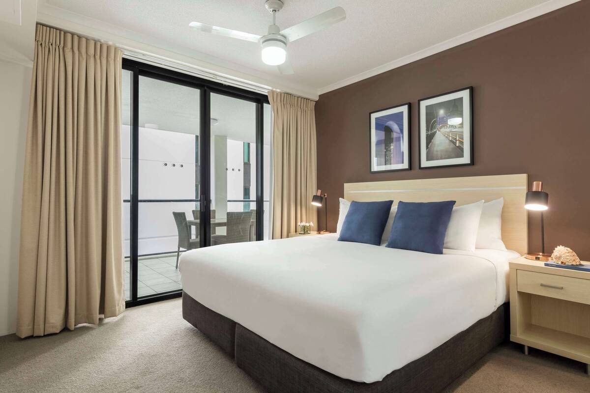 Ein Hotelzimmer mit einem großen Bett, einem Nachttisch, einer Lampe und einem Deckenventilator.