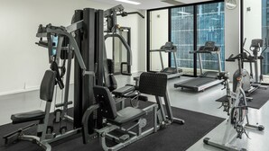 Une salle de sport équipée de divers appareils d’exercice, notamment des tapis de course et des appareils de musculation, et dotée de grandes fenêtres offrant une vue sur la ville.