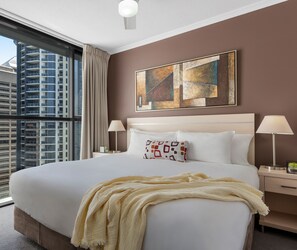 Habitación de hotel con una cama grande, dos lámparas de noche, una ventana con vista a un edificio alto y una obra de arte abstracto en la pared.