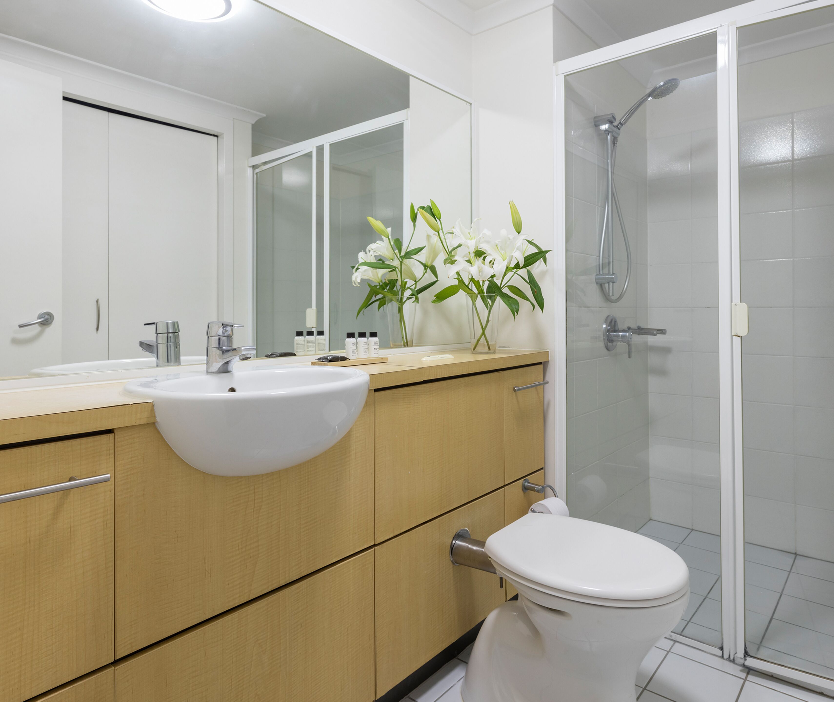 Een moderne badkamer met een witte wastafel, houten opbergmeubel, toilet en een douche met glazen wanden.