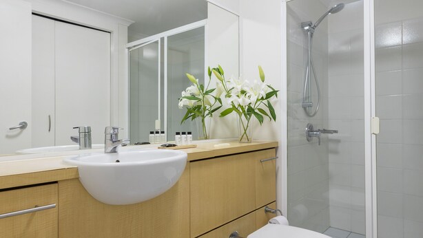 Une salle de bain moderne avec un lavabo blanc, un meuble-lavabo en bois, des toilettes et une douche à parois de verre.