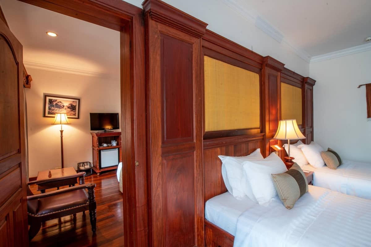 Una habitación de hotel con paneles de madera, una cama con ropa blanca, un escritorio con lámpara y un televisor.