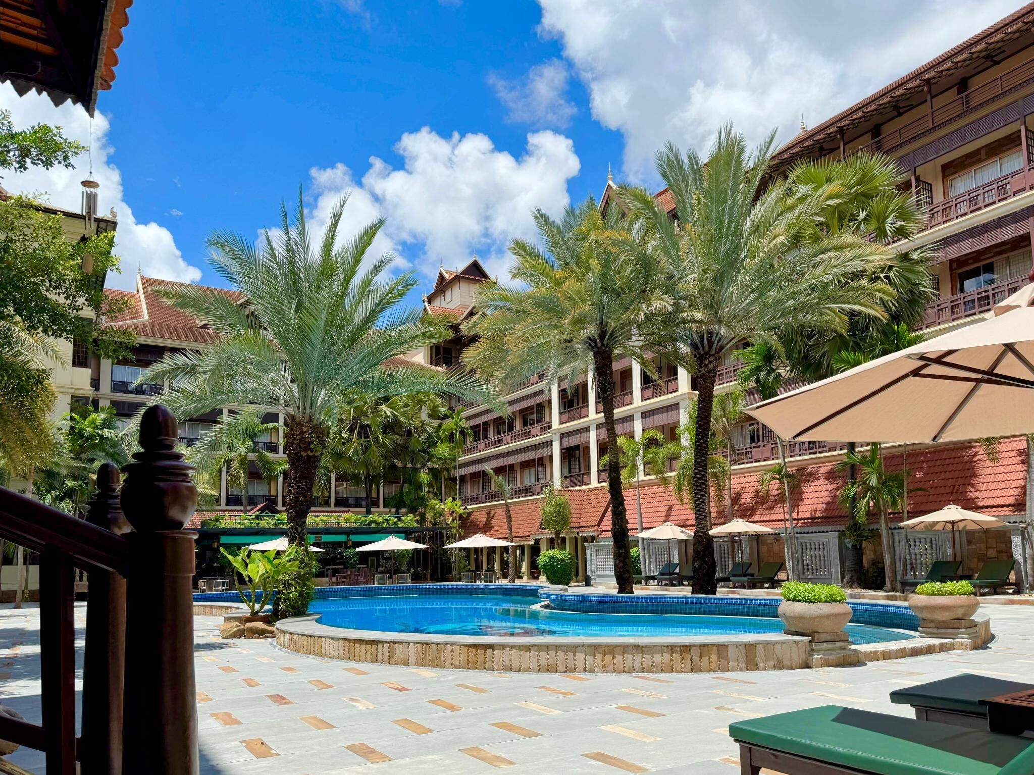 A hotel courtyard with a central swimming pool, palm trees, and outdoor seating areas.