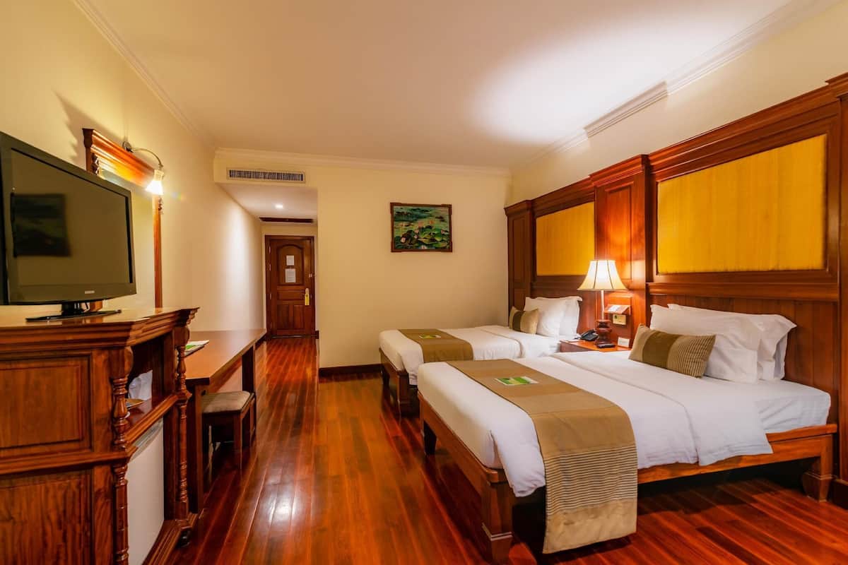 Habitación de hotel con dos camas, televisión, muebles de madera y un cuadro en la pared.