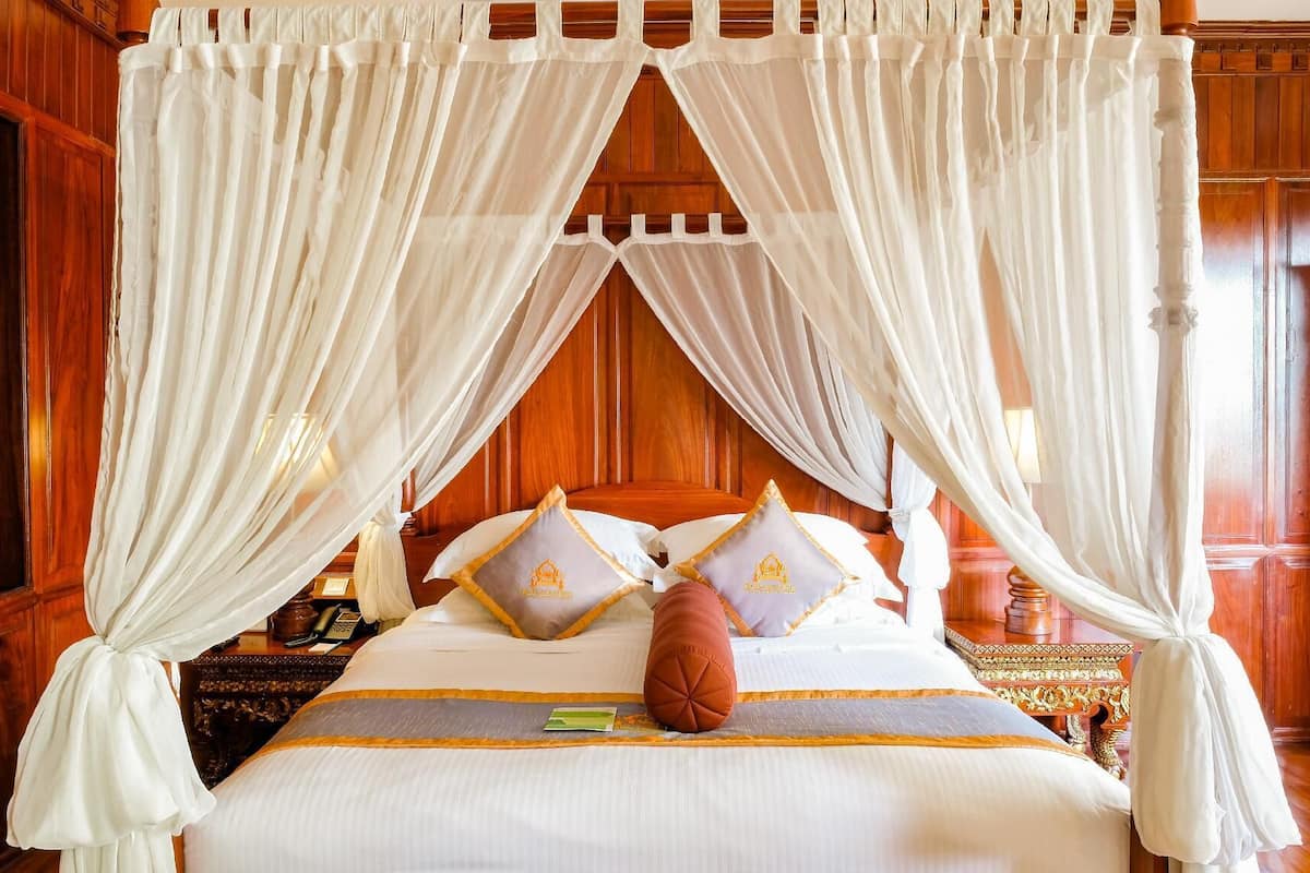 Una cama con dosel y cuatro columnas, con cabecera de madera, ropa de cama blanca y almohadas decorativas.