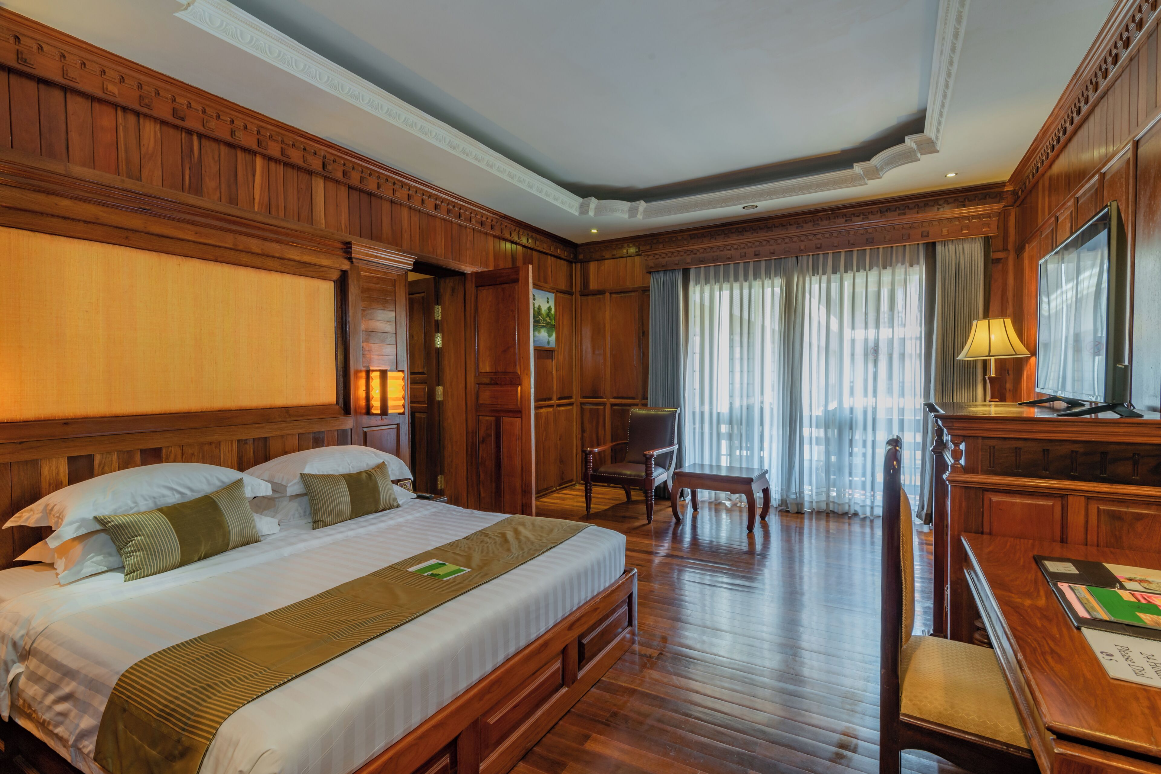 Quarto de hotel com uma cama grande, painéis de madeira, uma escrivaninha e uma cadeira.