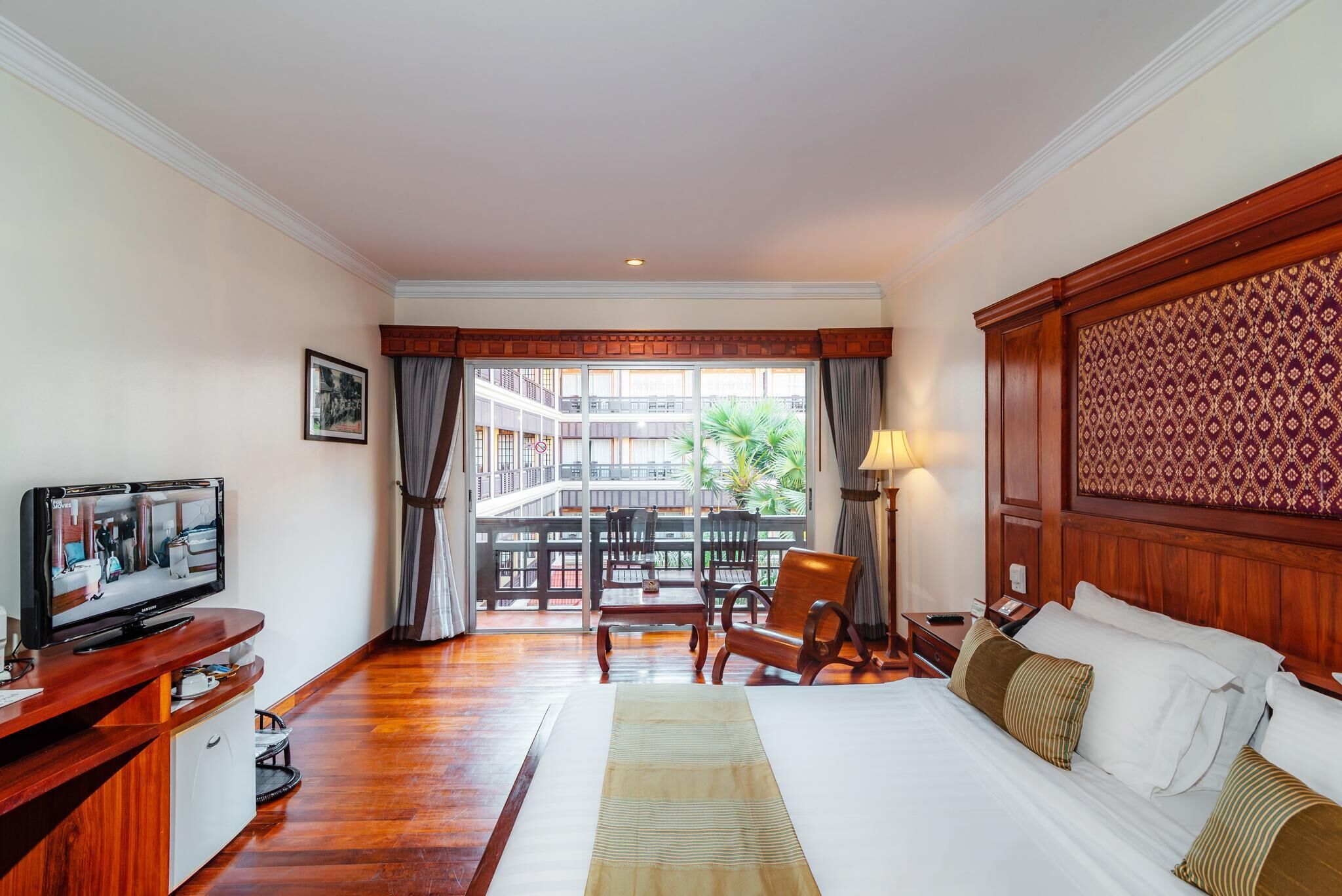 Habitación de hotel con cama, televisión, escritorio y balcón con vistas al exterior.