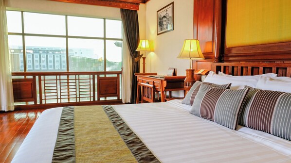 Habitación de hotel con una cama grande, un escritorio, una silla, una lámpara y vistas a edificios a través de la ventana.