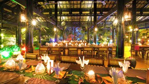 A restaurant with tables set for dining, illuminated by hanging lanterns and candles, with a view of greenery outside. - Empress Angkor Resort & Spa (Siem Reap)