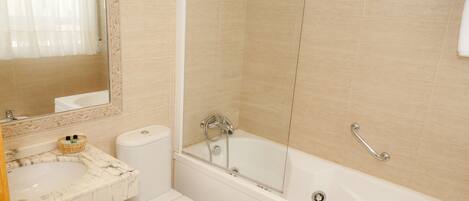 Un baño con lavamanos de mármol, inodoro y bañera con puerta de vidrio.