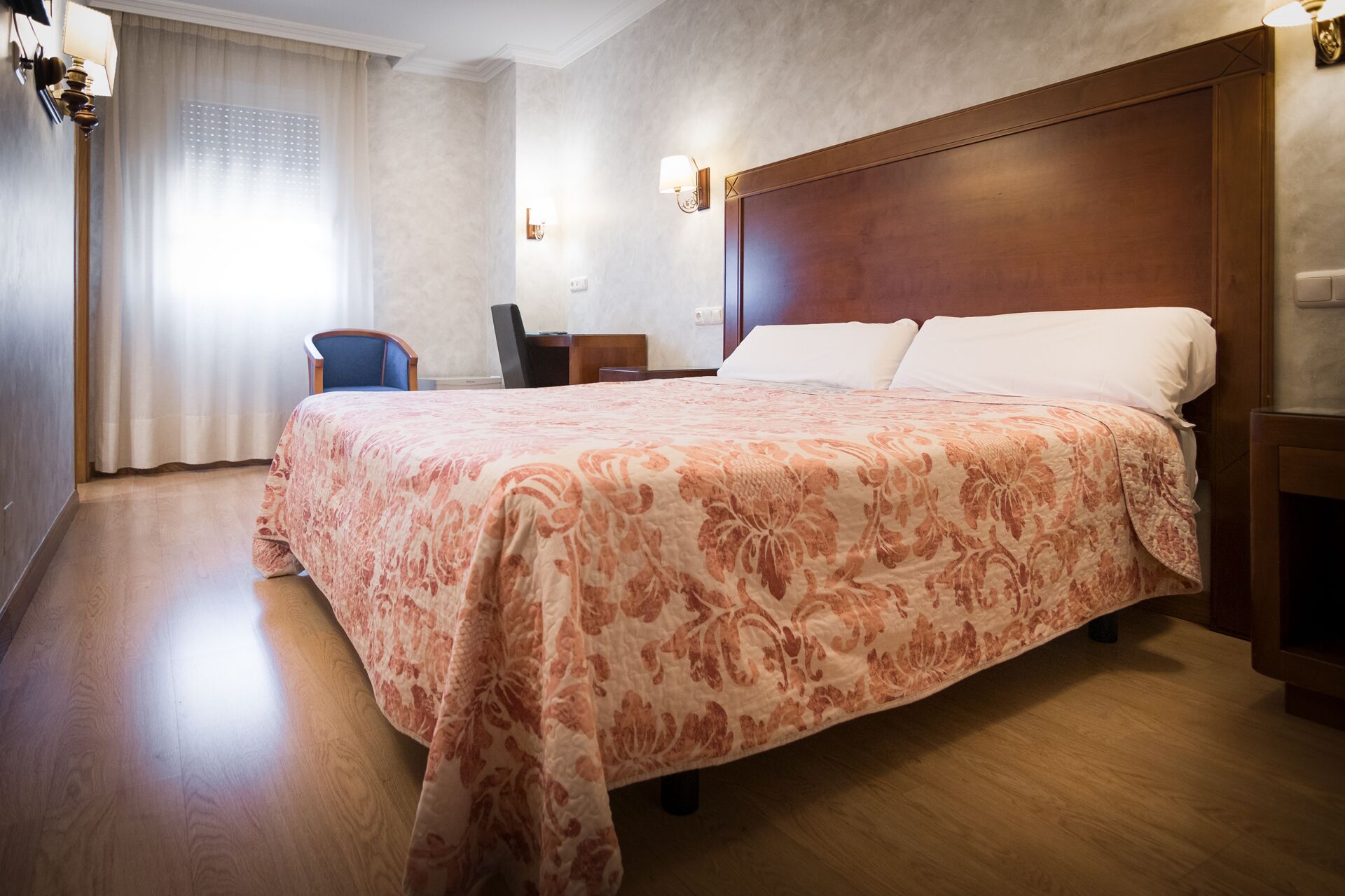 A hotel room with a large bed, a desk, a chair, and a window with curtains.