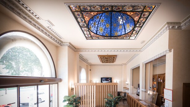 Un vestíbulo de hotel con techo alto, un gran ventanal de vitral y una recepción.