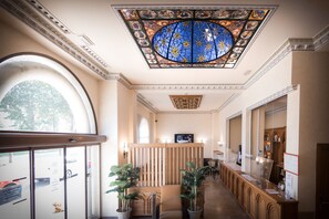 Eine Hotelhalle mit hoher Decke, einem großen Buntglasfenster und einer Rezeption.