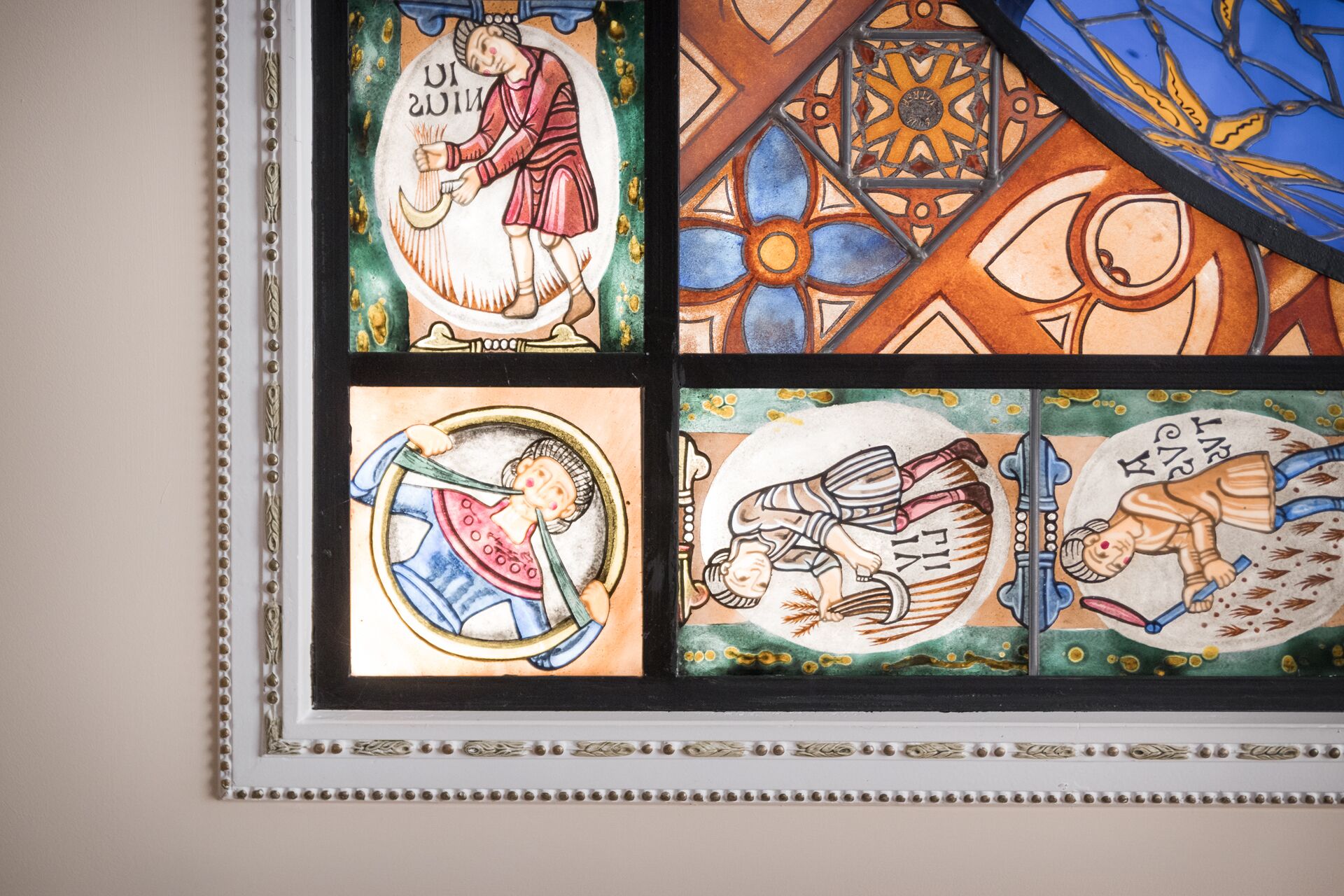 Een glas-in-loodraam met vier panelen waarop religieuze taferelen zijn afgebeeld.