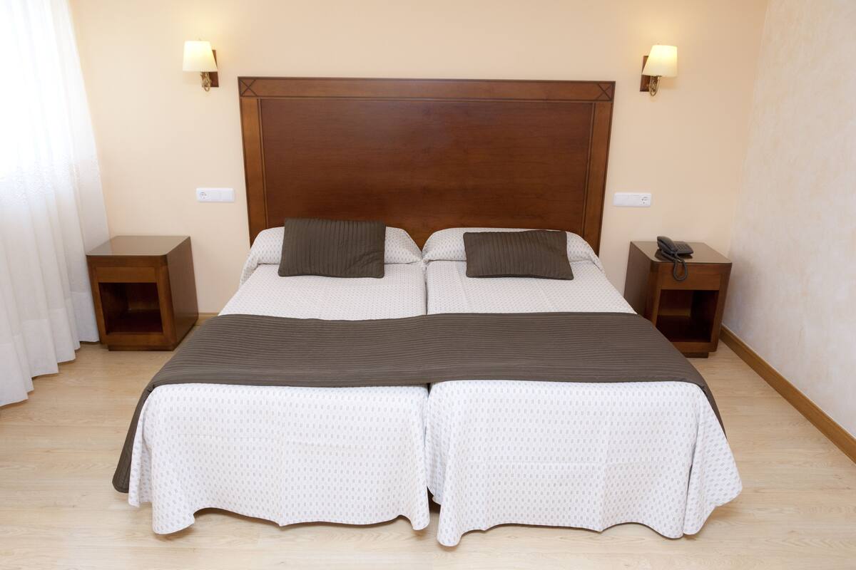 Una cama doble con cabecera de madera, dos mesitas de noche y dos lámparas de pared.
