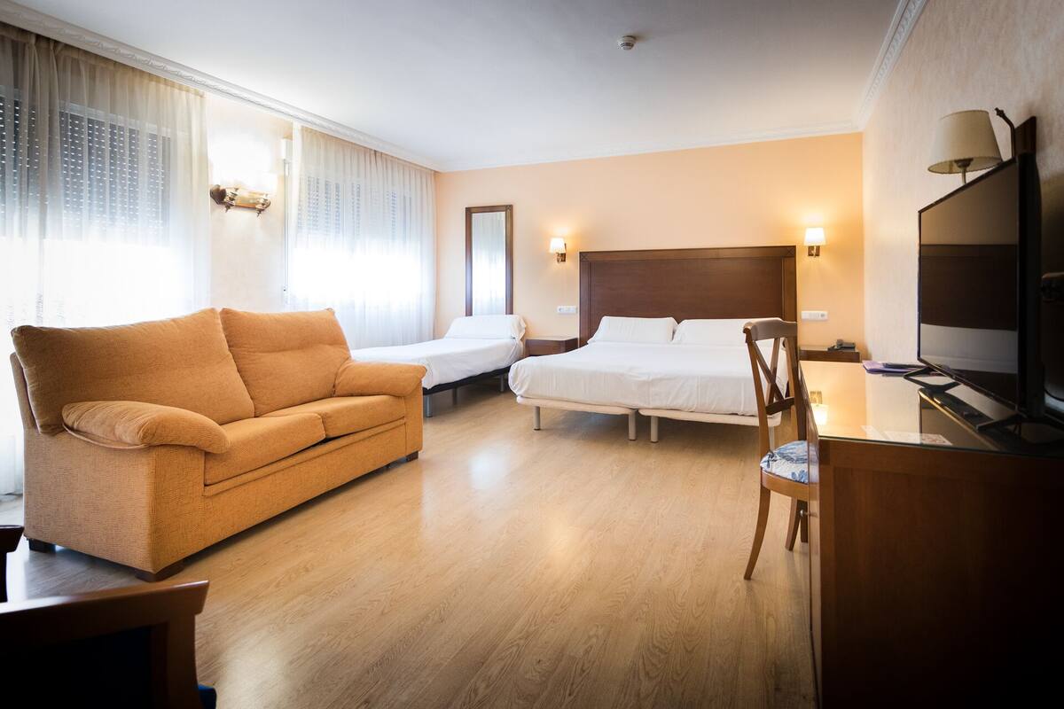 Una habitación de hotel con sofá, cama, escritorio y silla, y un televisor.