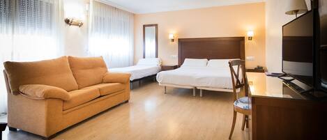 A hotel room with a sofa, a bed, a desk with a chair, and a television.