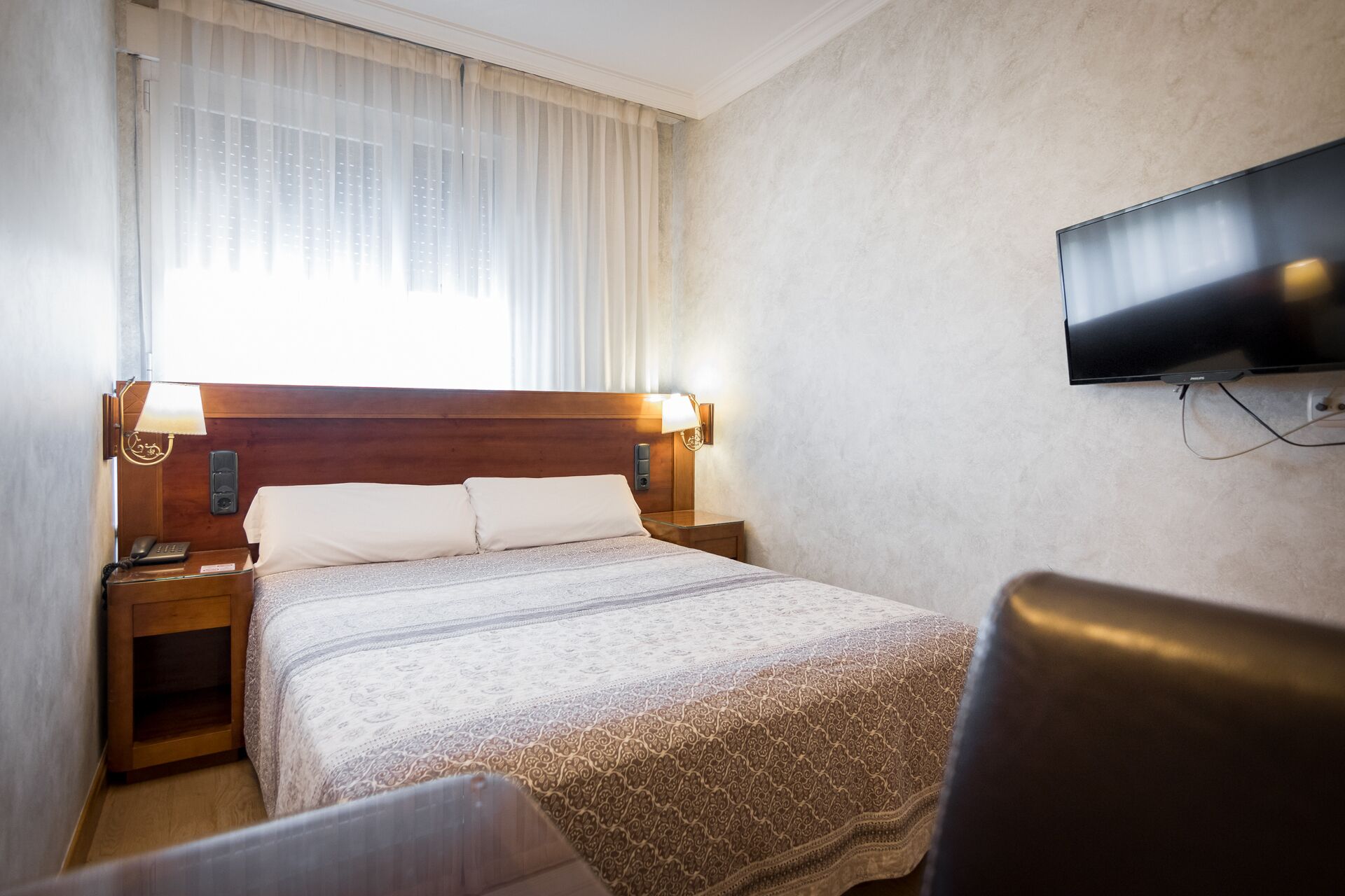 Una habitación de hotel con cama, mesitas de noche, televisión y una silla.