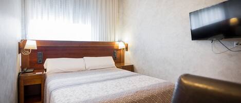 Una habitación de hotel con cama, mesitas de noche, televisión y una silla.