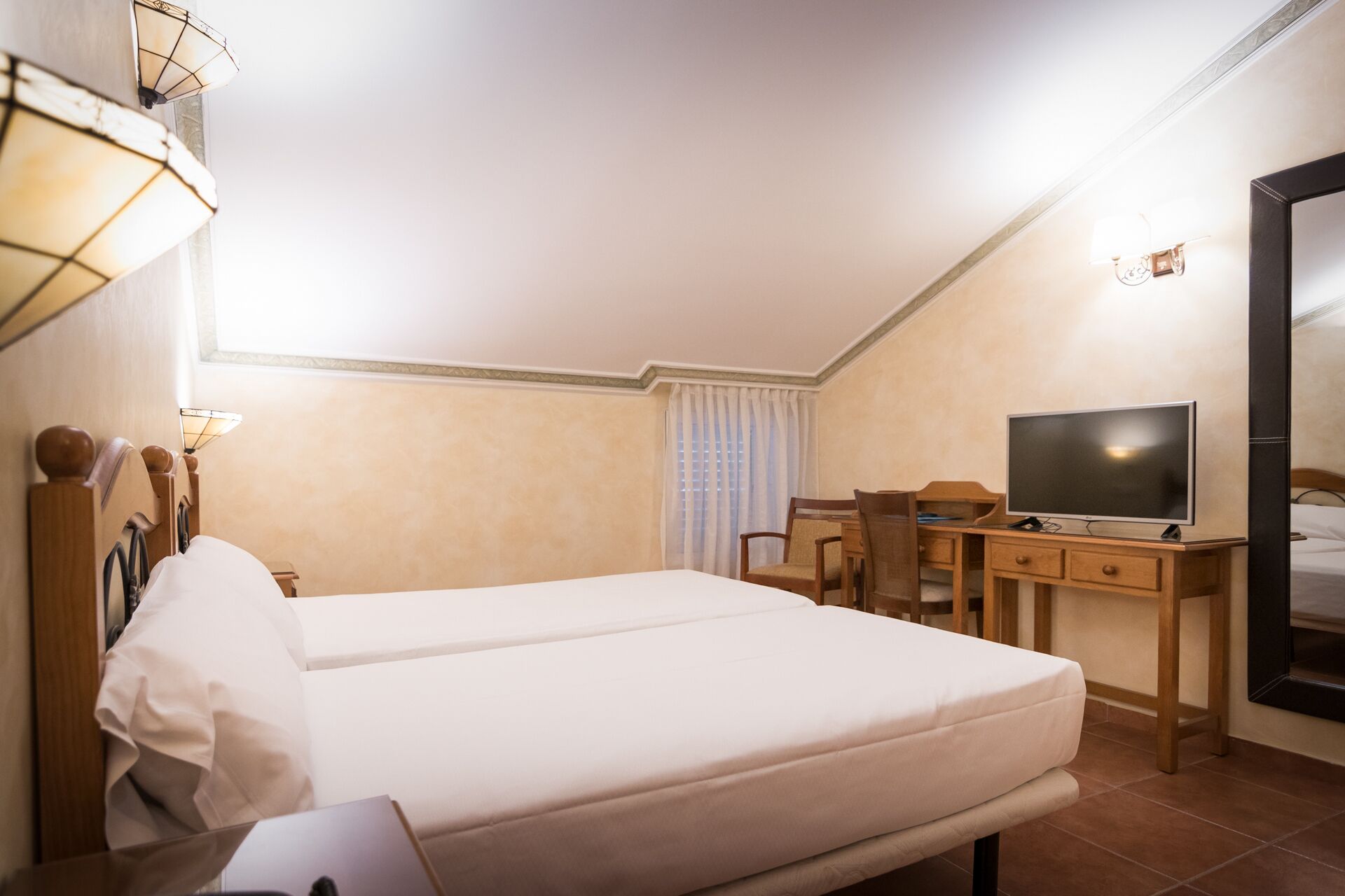 Hotelkamer met een bed, bureau, stoel, televisie en raam met gordijnen.