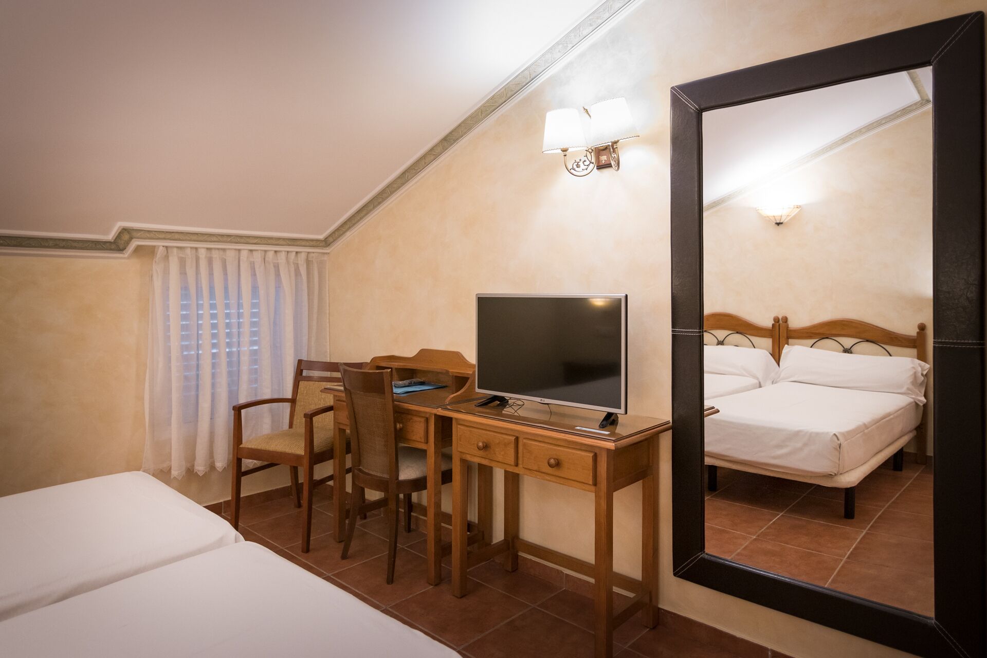 A hotel room with a desk, two chairs, a bed, and a large mirror.