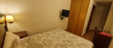 Un dormitorio con cama, mesita de noche con lámpara, televisor montado en la pared y armario.