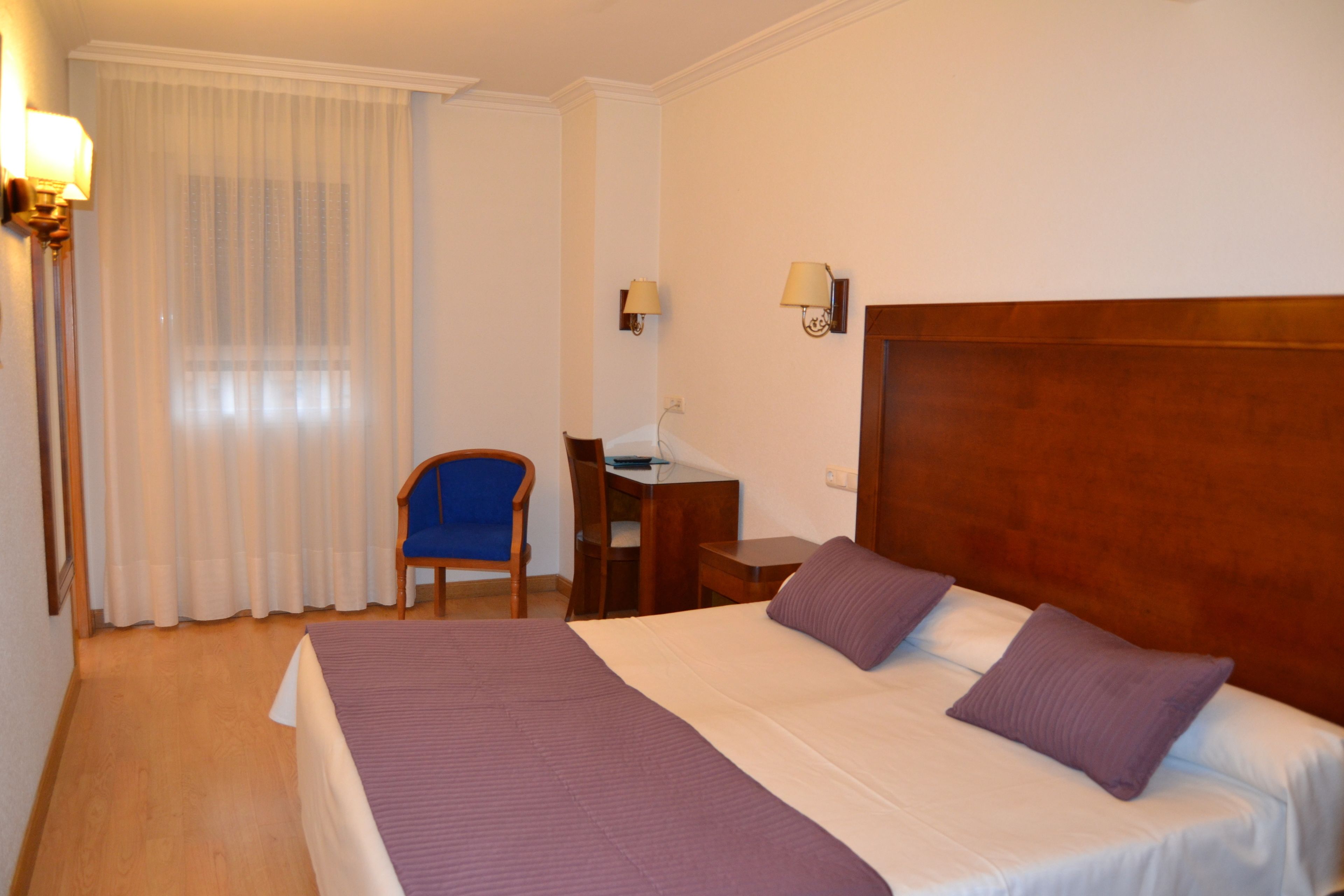 Een hotelkamer met een groot bed, een bureau, een stoel en een raam met gordijnen.