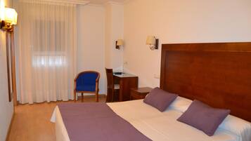 Een hotelkamer met een groot bed, een bureau, een stoel en een raam met gordijnen.