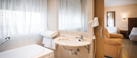 A modern bathroom with a bathtub, sink, and a mirror. There is a towel rack with folded towels and a hairdryer on the wall.