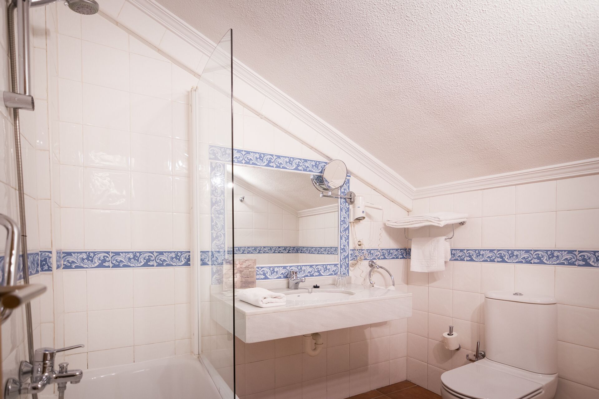 Une salle de bain avec une douche à parois de verre, un lavabo avec un miroir, des toilettes et des carreaux bleus décoratifs.