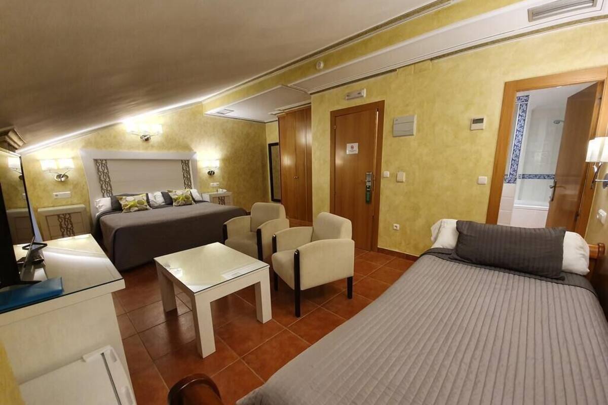 Habitación de hotel con cama, escritorio, silla y una mesita. Hay dos puertas: una que da al baño y otra a un armario.