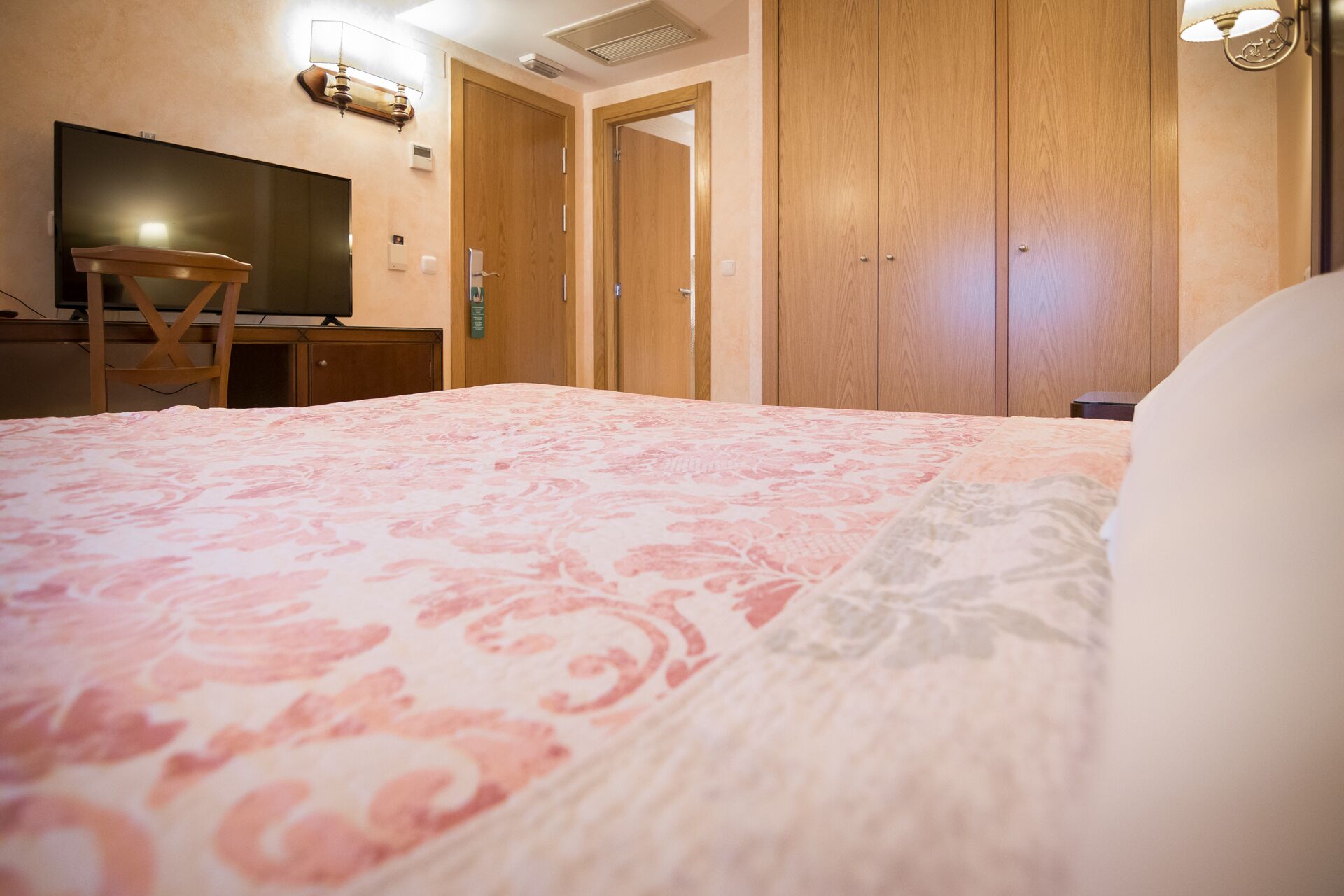 A hotel room with a bed, a desk, a chair, and a television.