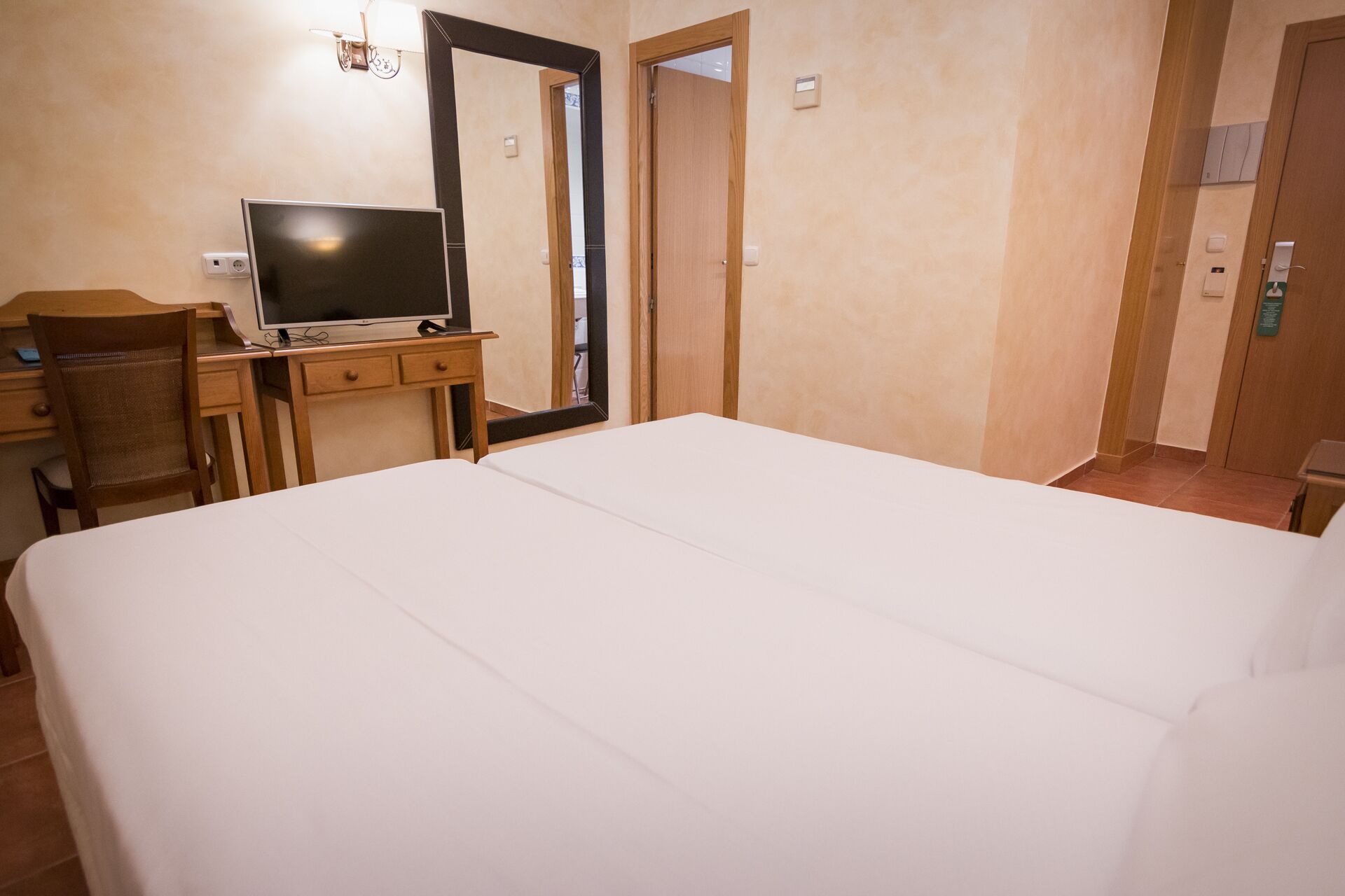 A hotel room with a bed, a desk, a chair, a television, and a mirror.