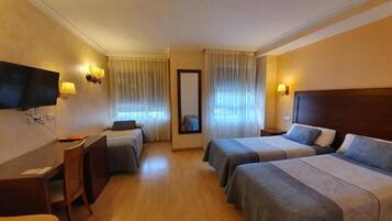 Habitación de hotel con dos camas, un escritorio, una silla, un televisor y dos lámparas de pared.