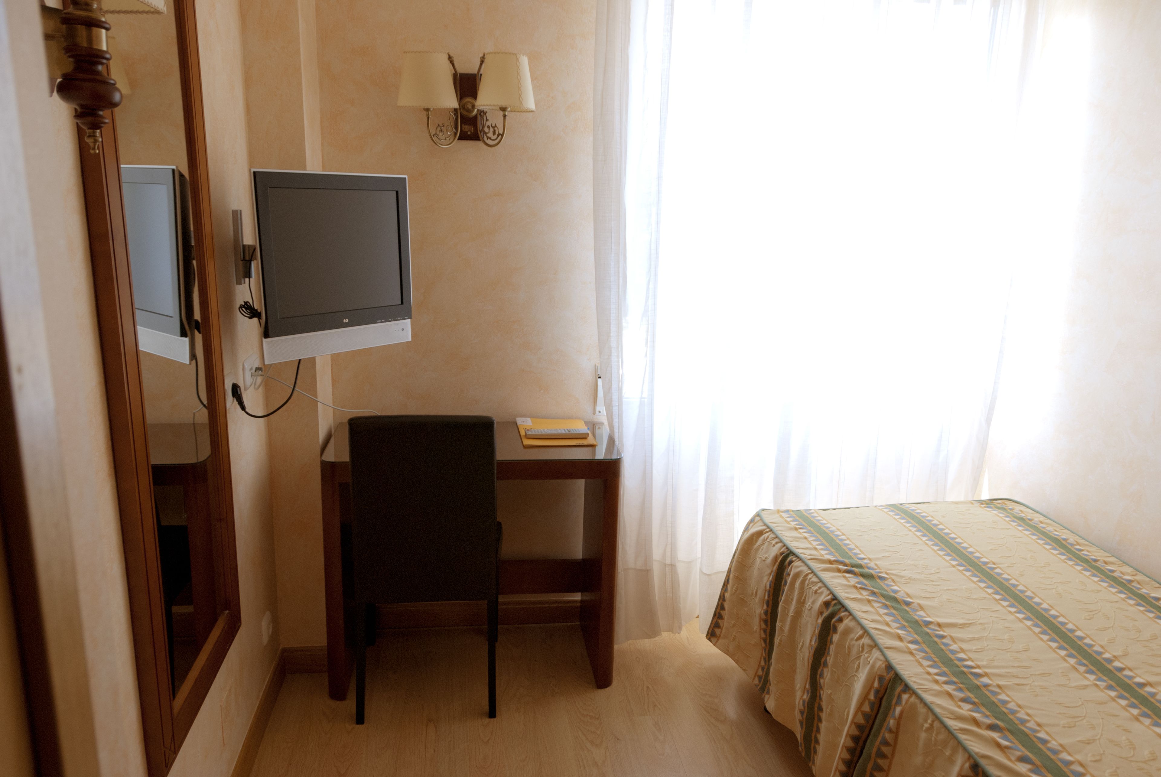 Una habitación de hotel con cama, escritorio con silla, televisor y lámpara.