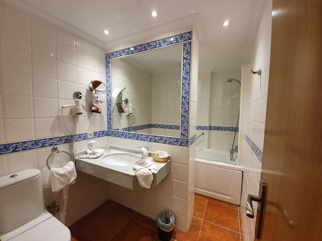 A bathroom with a white sink, mirror, and toilet, a shower area, and blue decorative tiles.