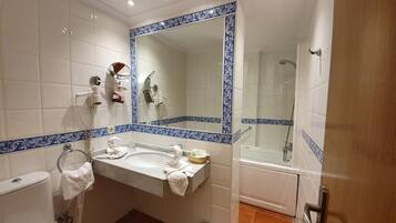 Un baño con lavamanos blanco, espejo, inodoro, zona de ducha y azulejos decorativos azules.