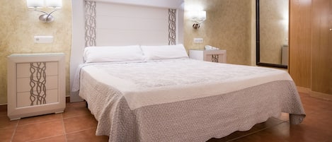 A neatly made bed with a textured blanket, a white headboard, and wall-mounted lights.