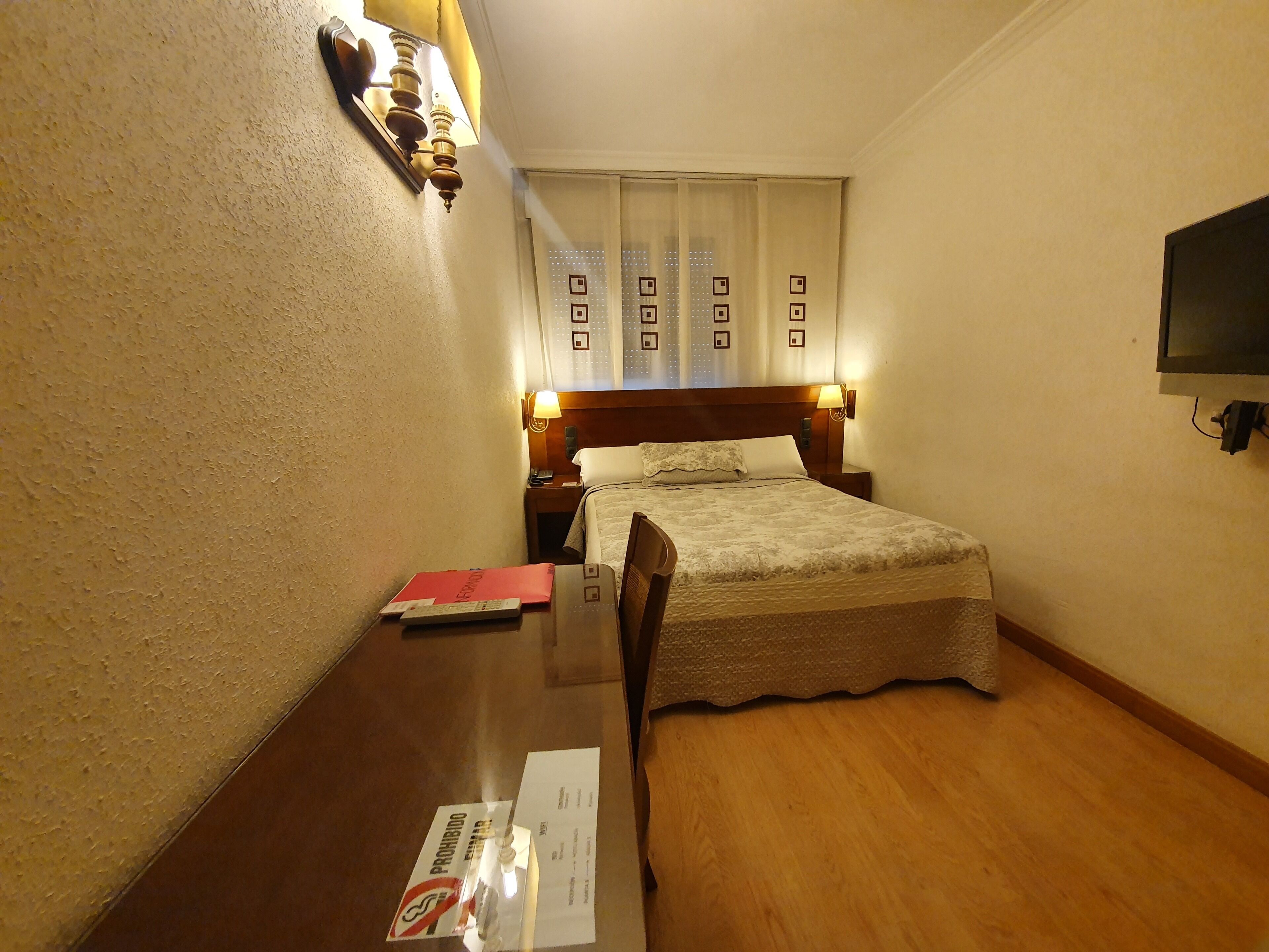 Une chambre d’hôtel avec un lit, des tables de chevet, un téléviseur fixé au mur et une fenêtre avec des rideaux.