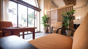 Un hall de hotel con mostrador de recepción, zona de estar y grandes ventanales con vista a la calle.