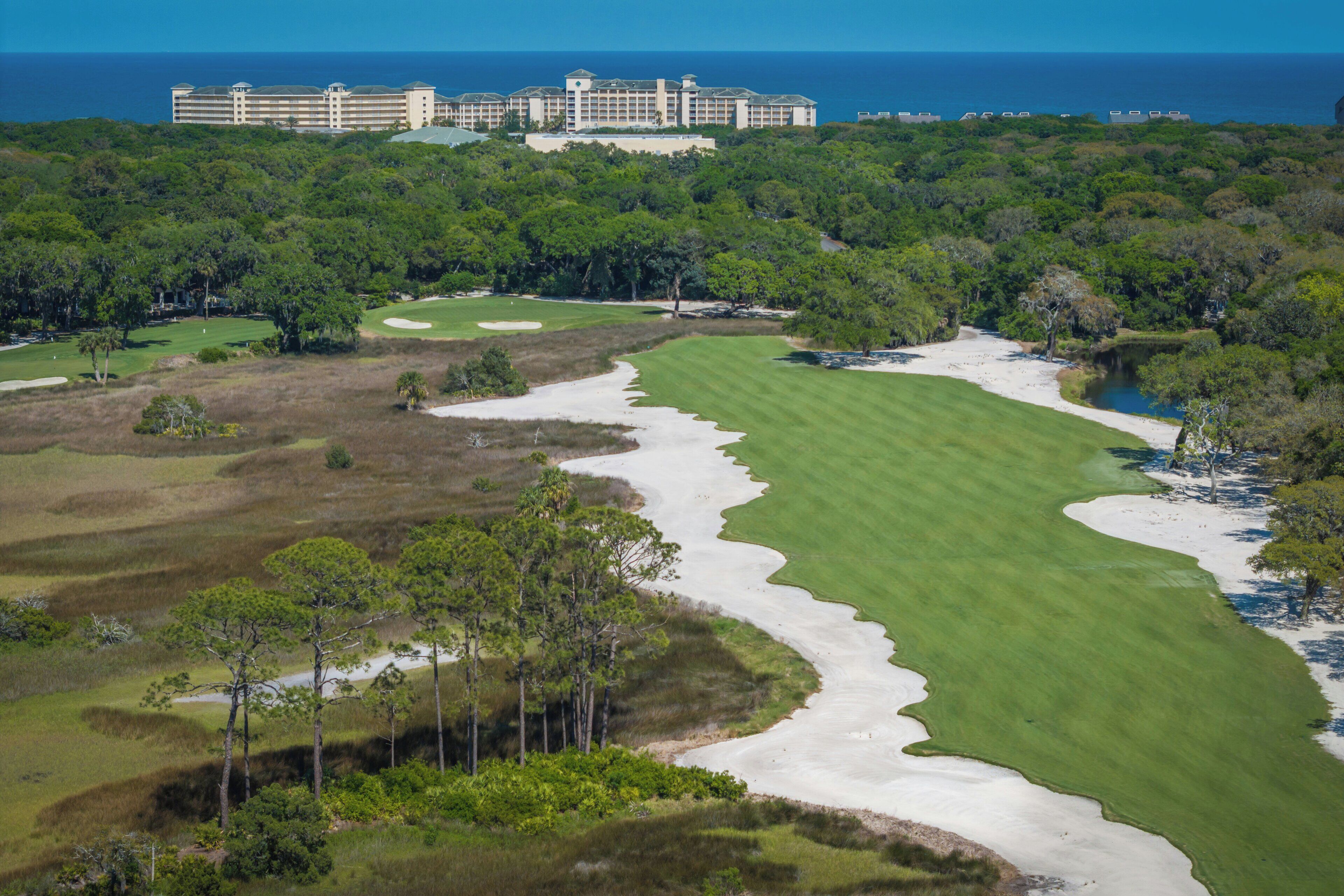 A golf course with sand bunkers, a water hazard, and a large hotel in the background.