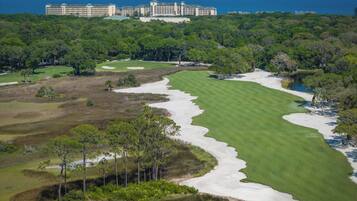 A golf course with sand bunkers, a water hazard, and a large hotel in the background.