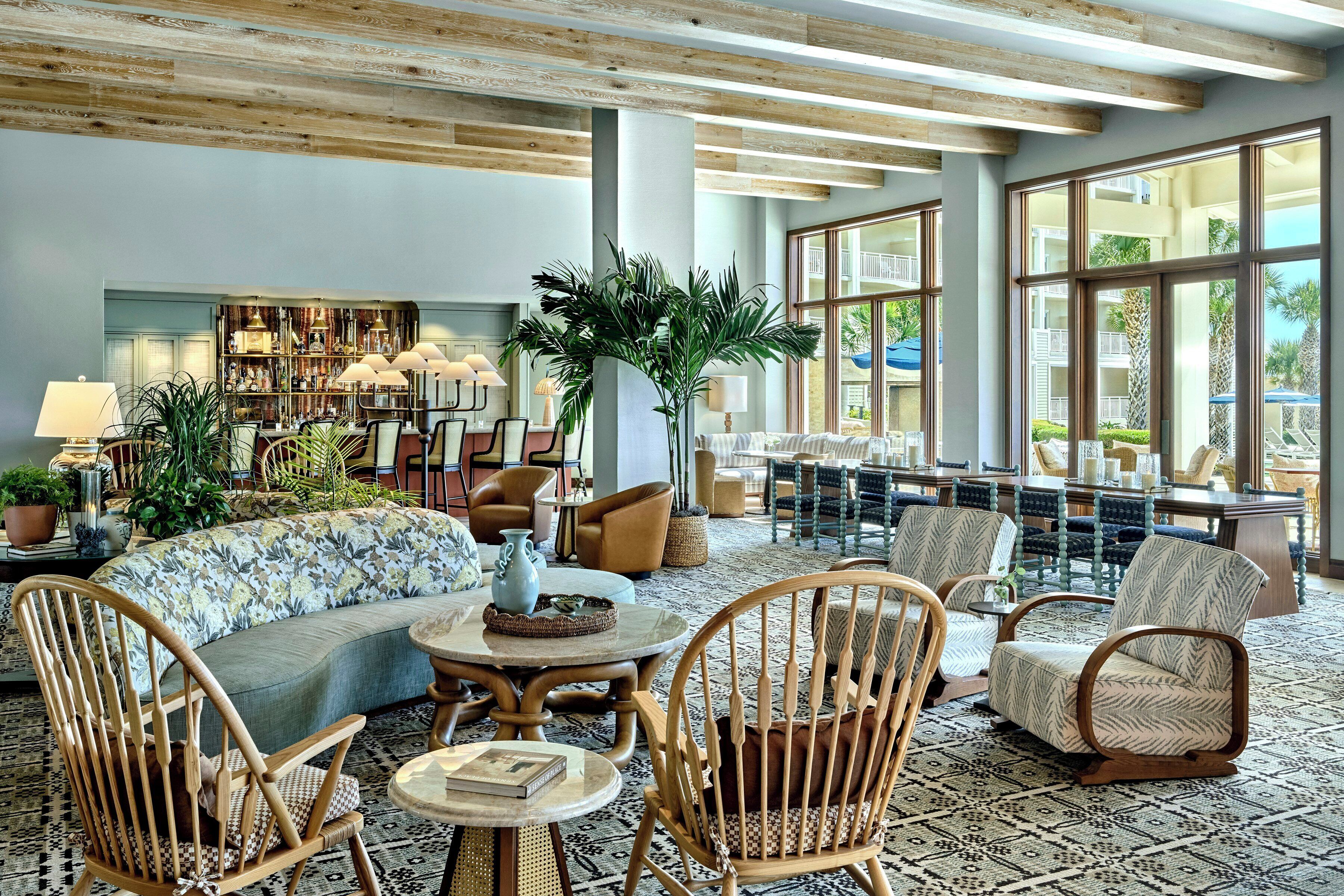 A spacious lobby with a high ceiling, large windows, a central seating area with sofas and chairs, and a bookshelf filled with books and decorative items.