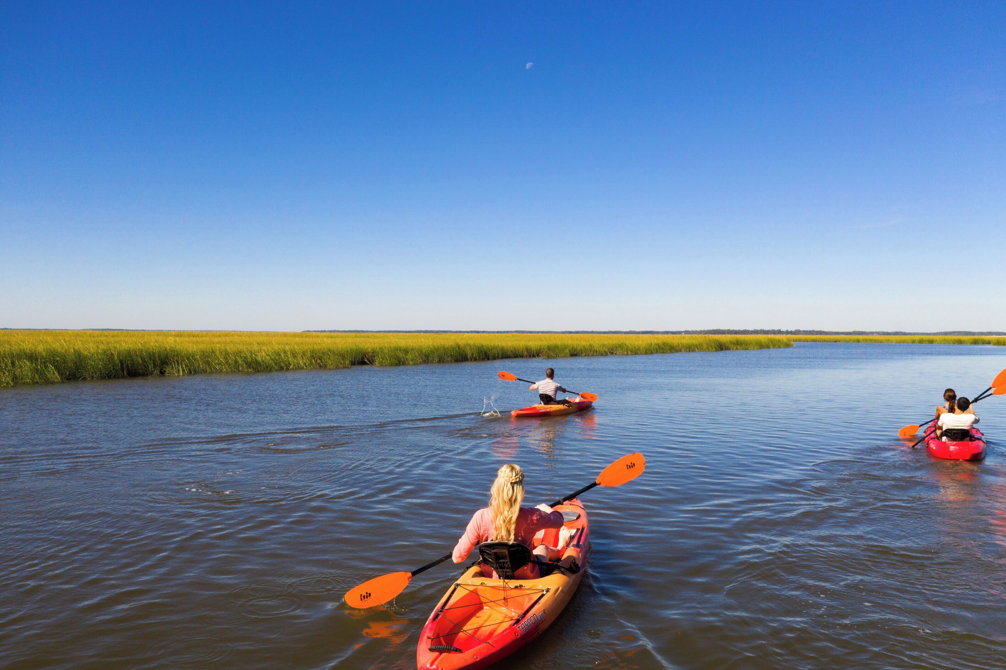 Three kayaks on a calm river with a clear sky.