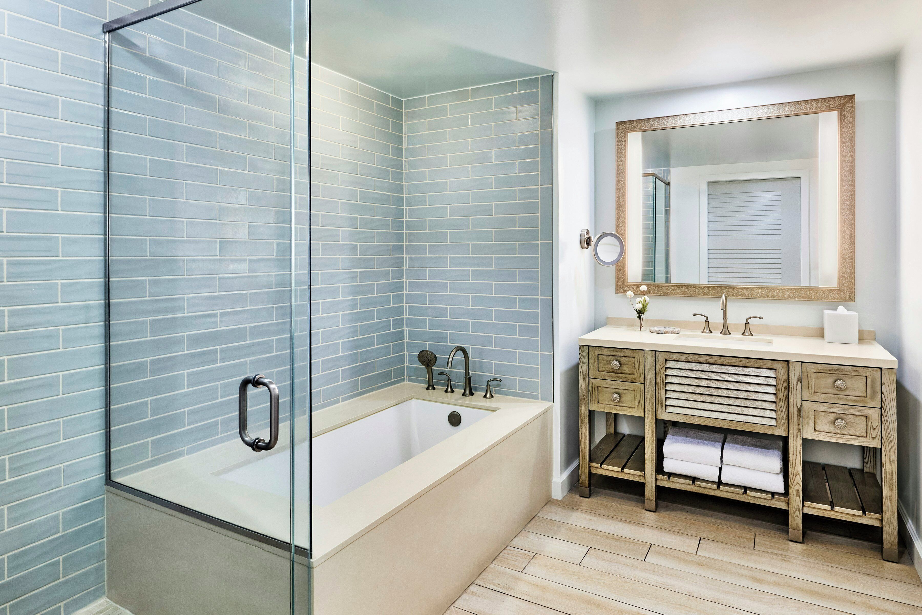 Un baño con cabina de ducha de vidrio, bañera, tocador con espejo y tocador de madera con cajones.