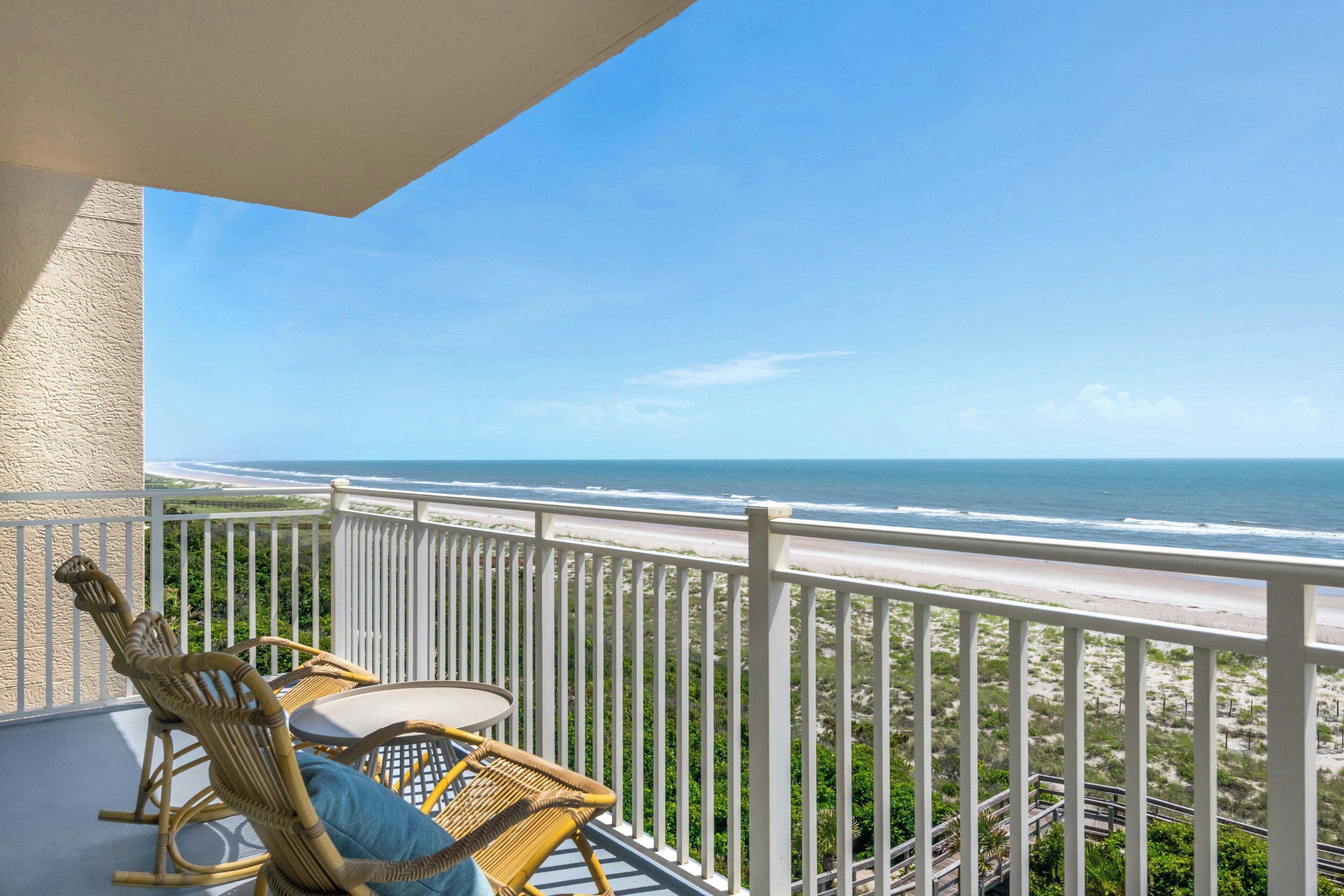 A balcony with wicker chairs and a table overlooking a beach.