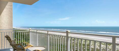 A balcony with wicker chairs and a table overlooking a beach.