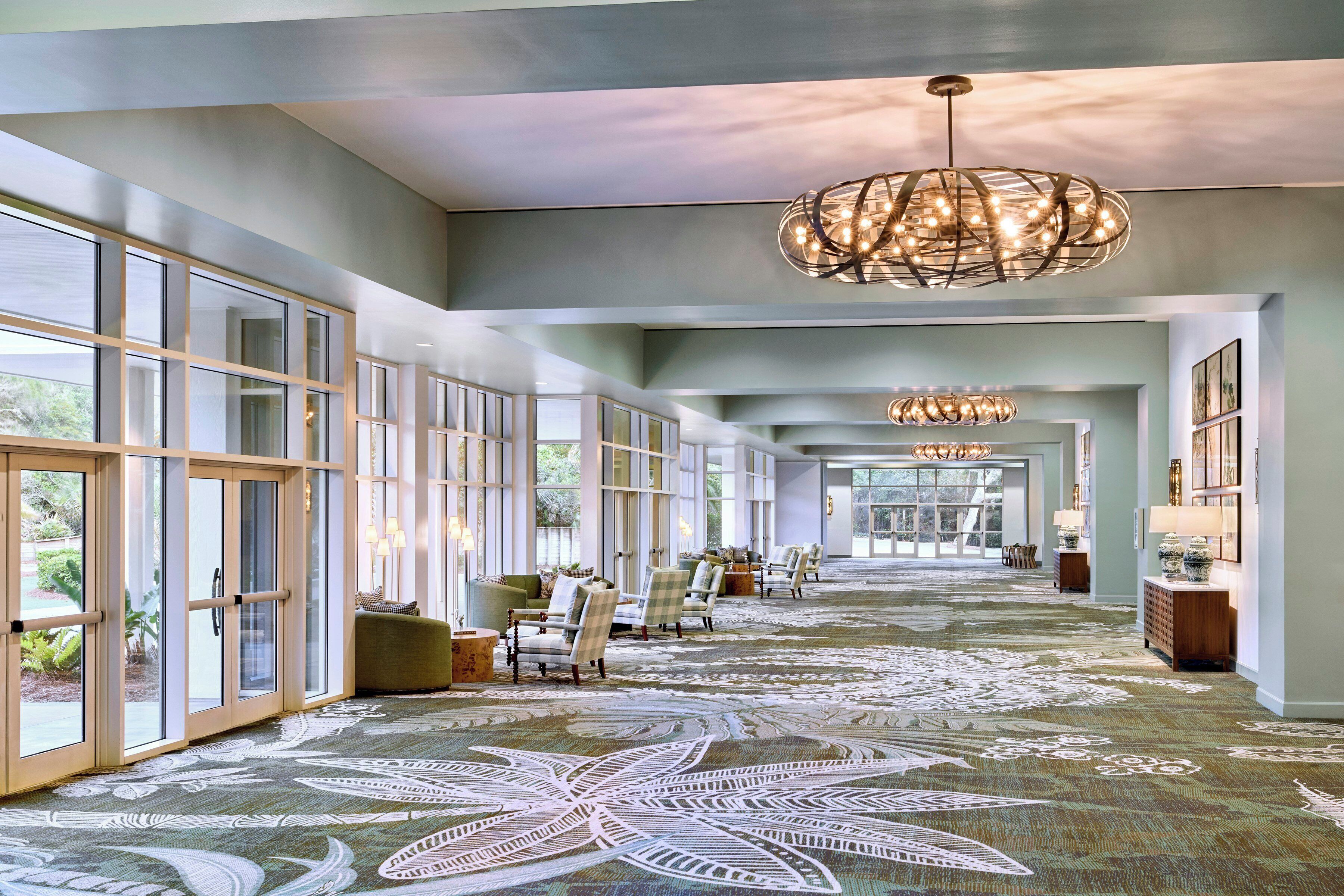A spacious hotel lobby with large windows, a patterned carpet, and multiple seating areas.