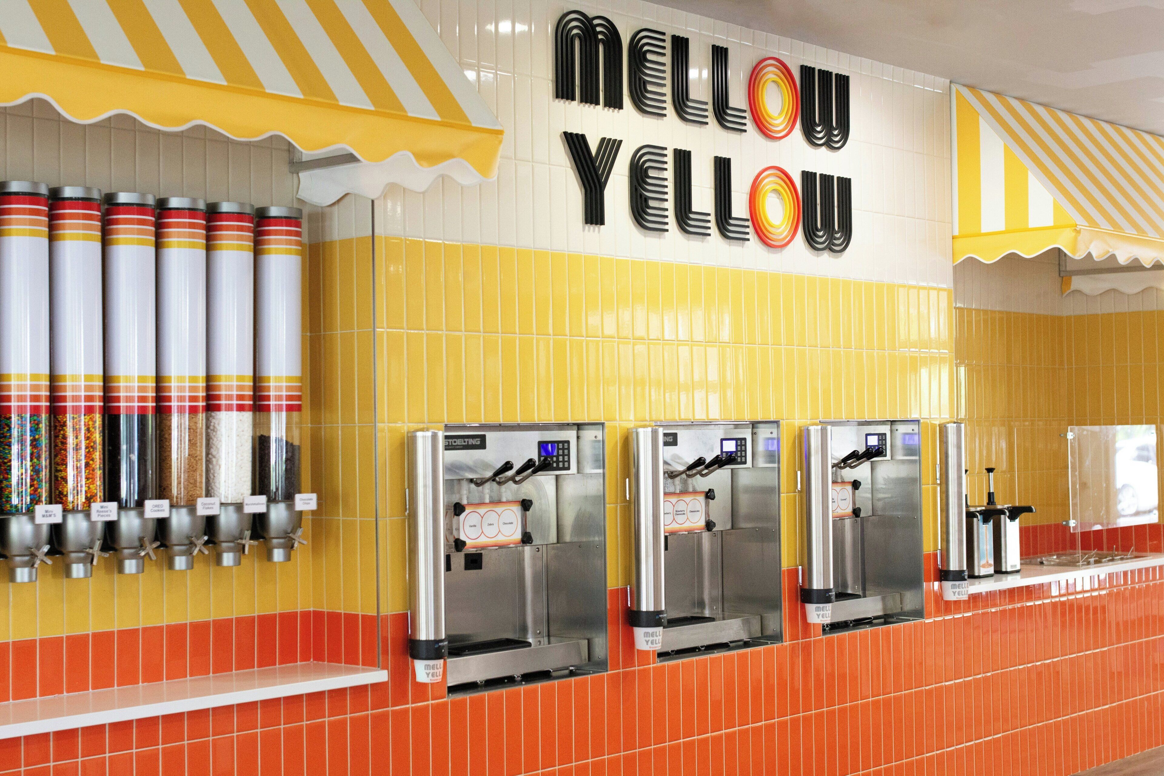 A wall with a yellow and orange tiled design, a sign that reads "MELLOYELLOW," and three beverage dispensers.