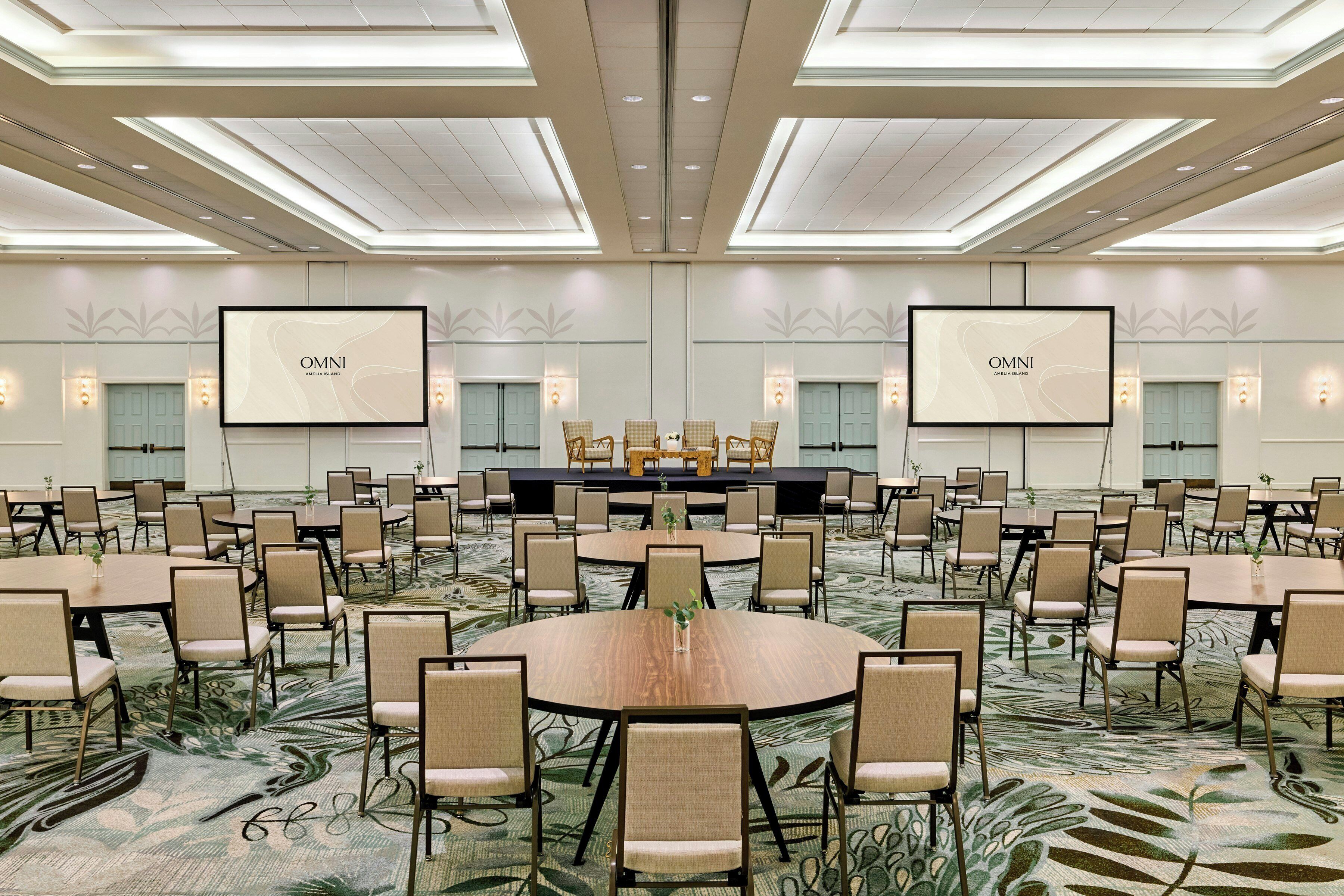 Un amplio salón de conferencias con varias mesas y sillas, un escenario y dos pantallas grandes mostrando 'OMNI'.